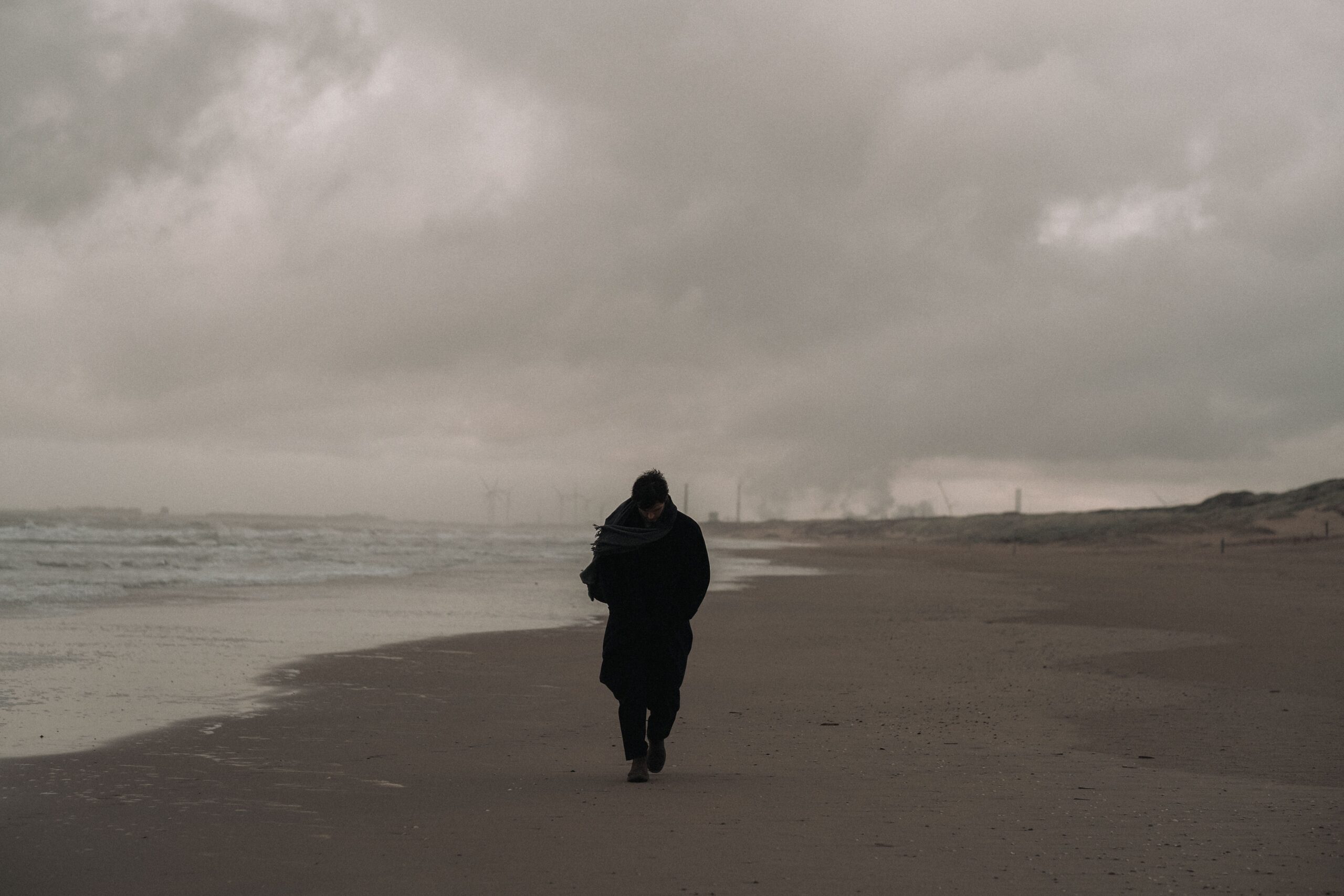 A person walks alone on a windy and overcast beach, creating a moody atmosphere.